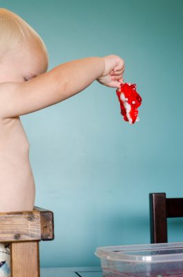 baby hesitantly pulling a toy pig out of jello while wearing a cloth diaper | This Indulgent Life