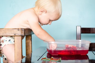 toddler hesitantly playing in jello while wearing a cloth diaper | This Indulgent Life