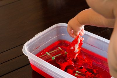 Pulling a plastic pig toy out of jello for a fun toddler sensory experience | This Indulgent Life